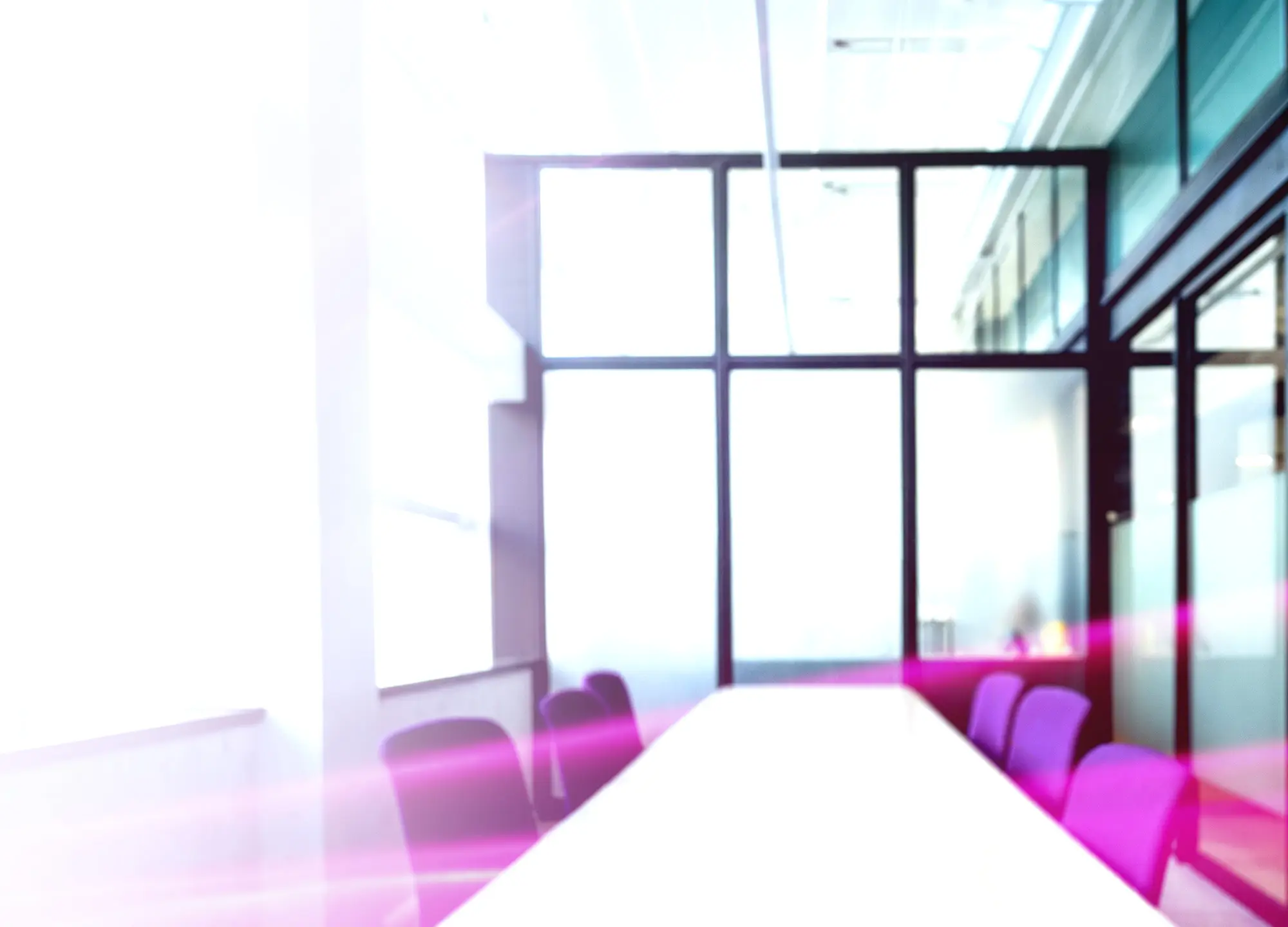 Bright, blurred conference room with a long white table, purple chairs, and large windows.