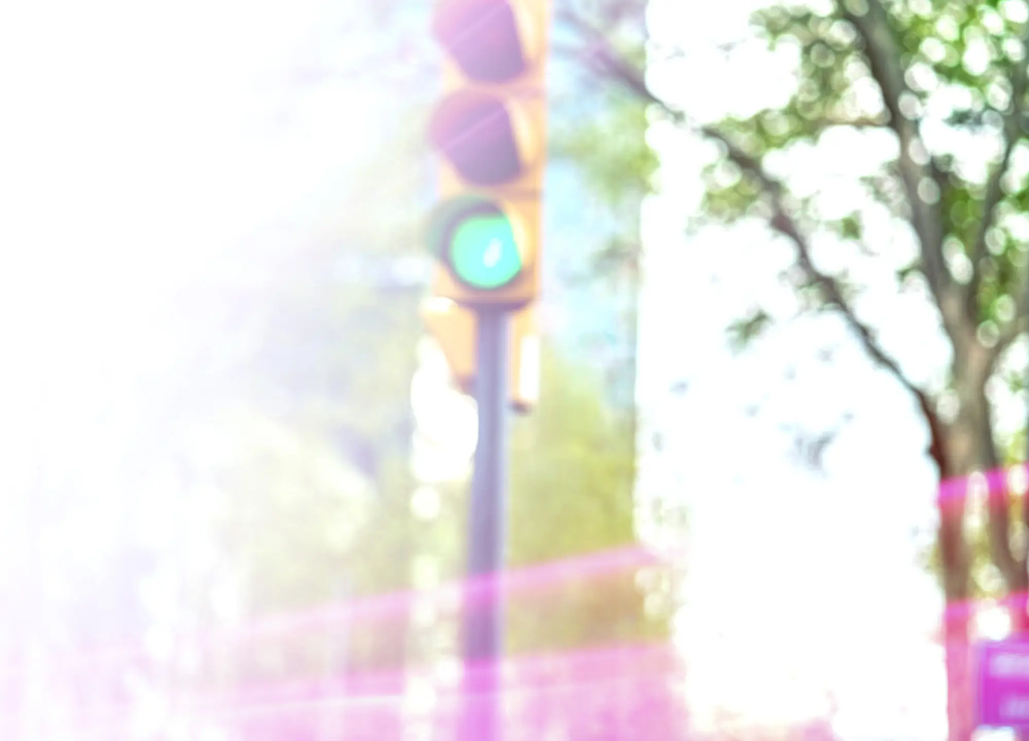 Blurred traffic light pole with the green signal illuminated, surrounded by bright light and purple lens flares.